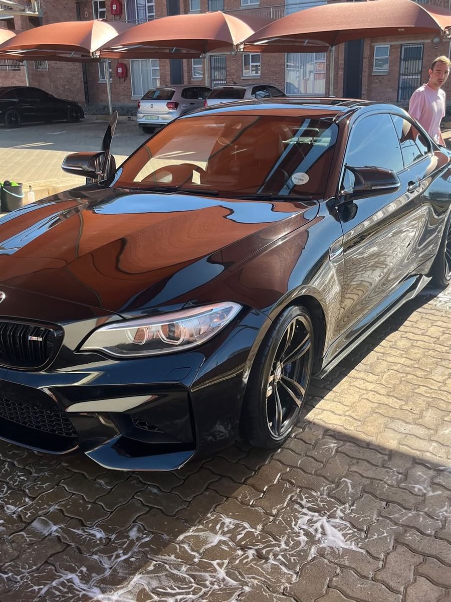 Black BMW M2 with glossy paint on wet paving after a wash
