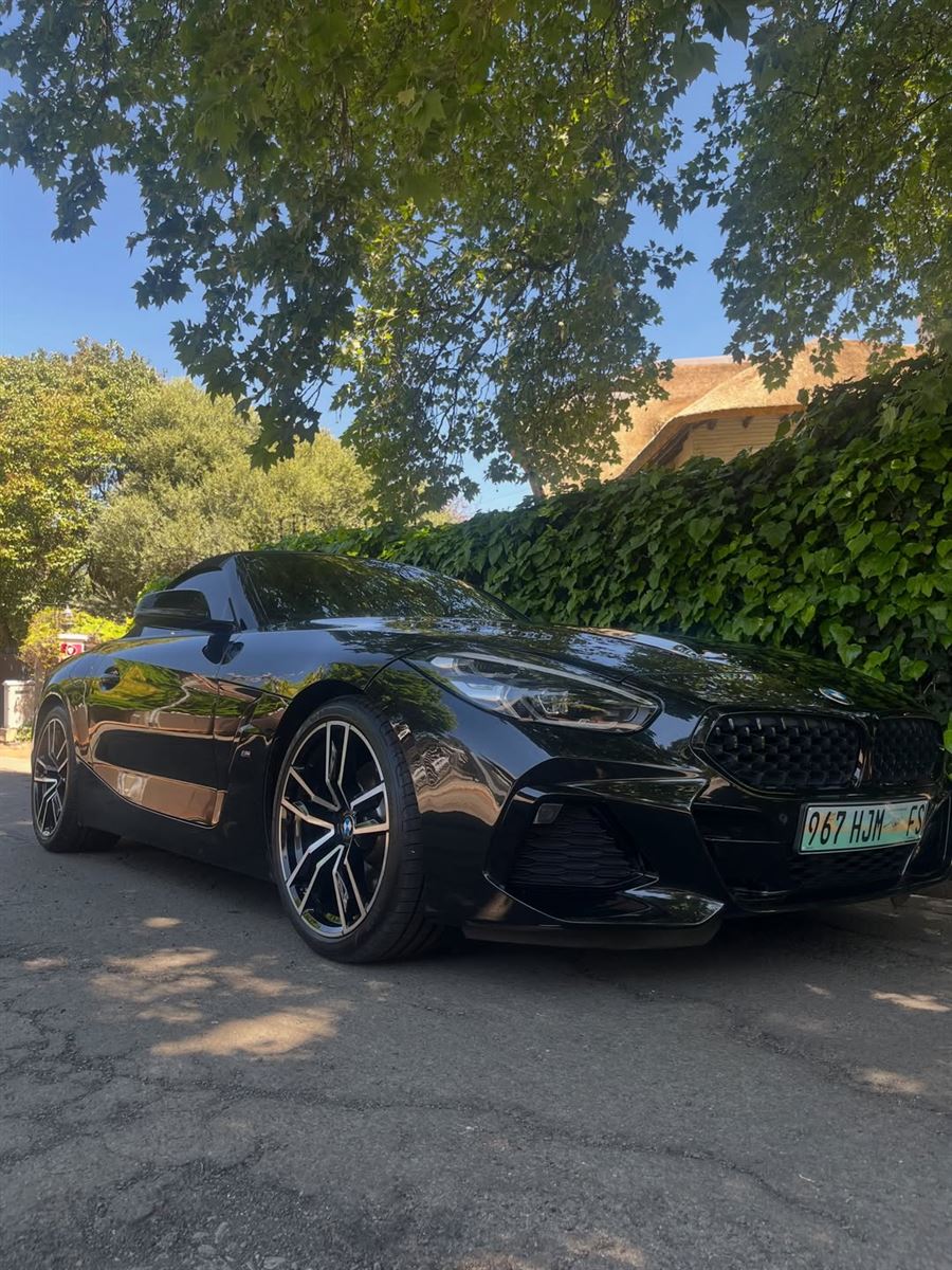 Black BMW Z4 roadster after a detail, parked under trees